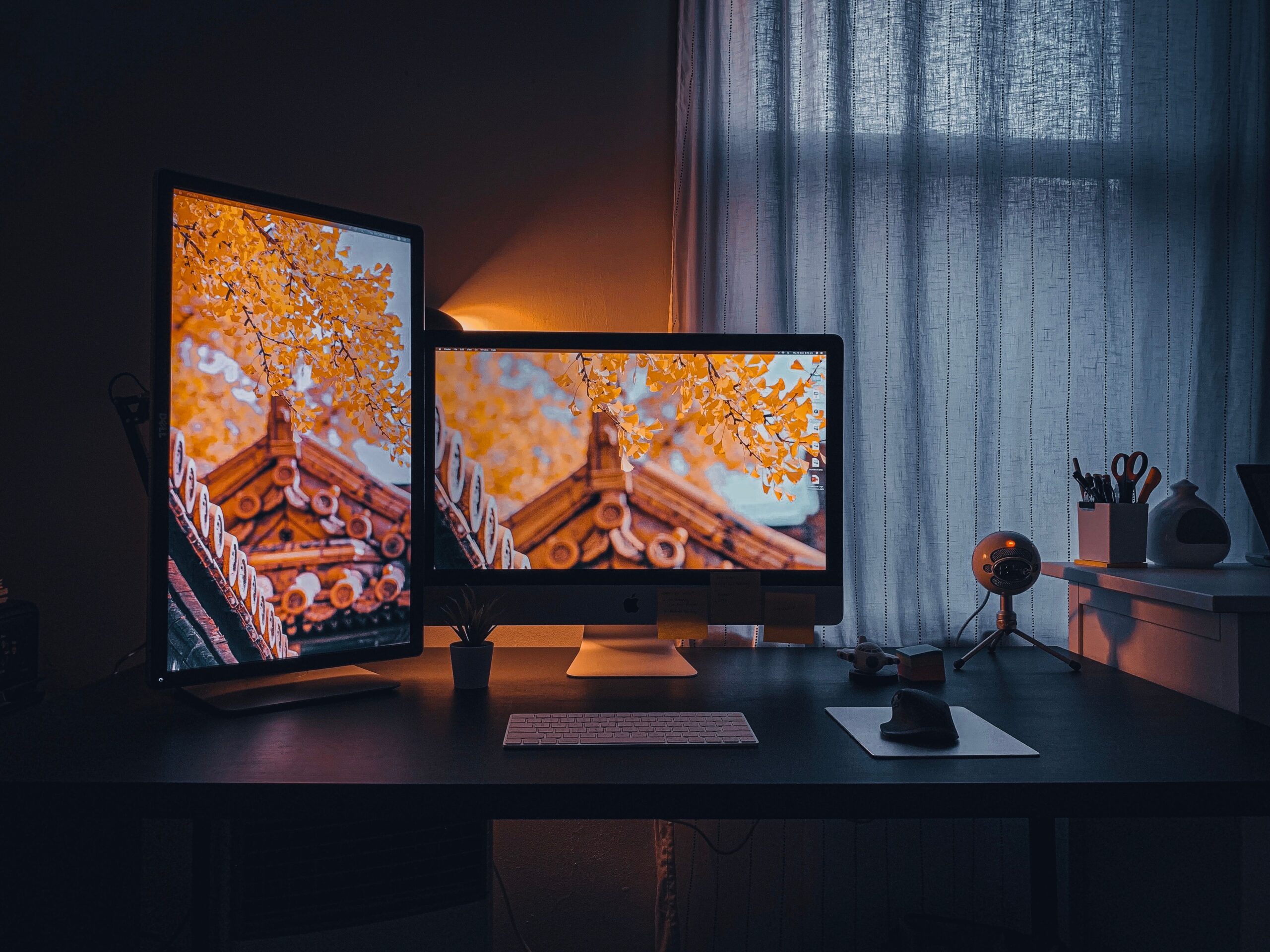 Desk setup with two computer monitors displaying an orange leaved temple roof image in a dimly lit room