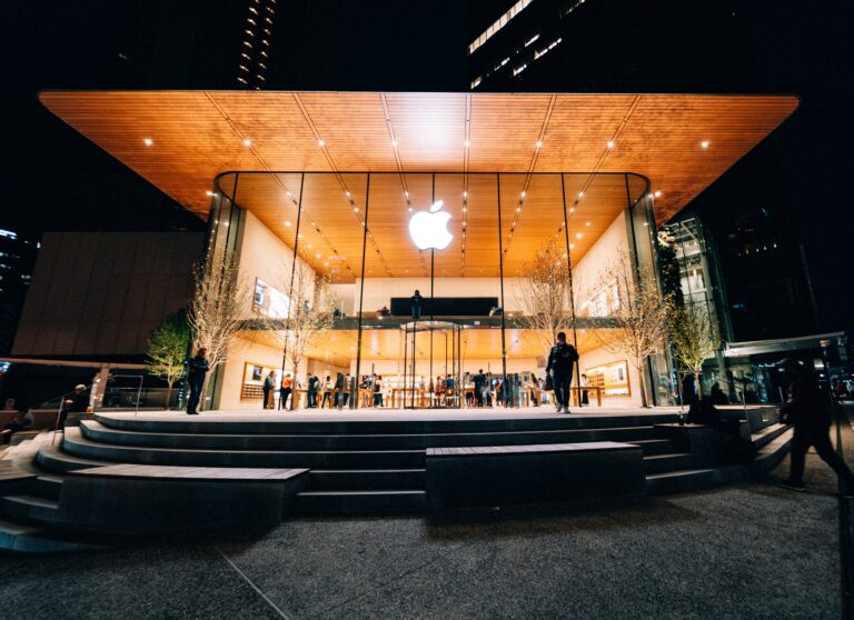 Night view of an Apple Store with a glass entrance warm wooden canopy and a glowing Apple logo visible inside