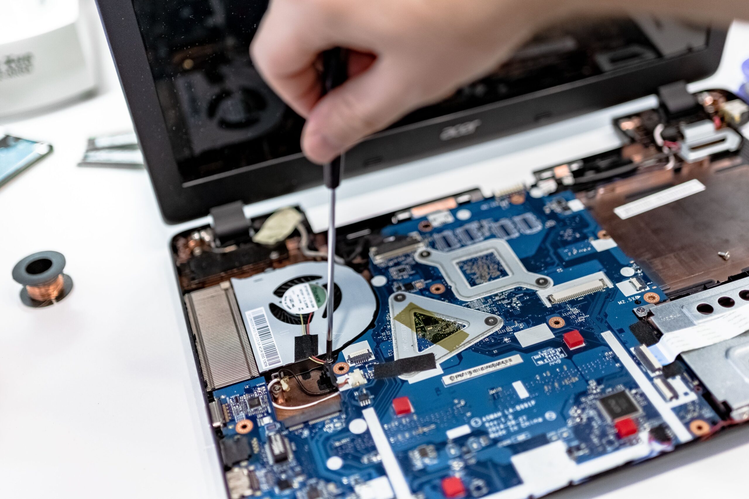 Close up of a technician using a tool to open a laptop exposing the motherboard and internal components including a cooling fan and copper wiring